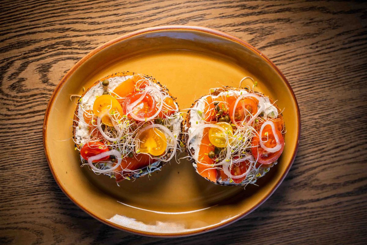 Open faced bagel sandwich with lox, cream cheese, tomato, and onion.