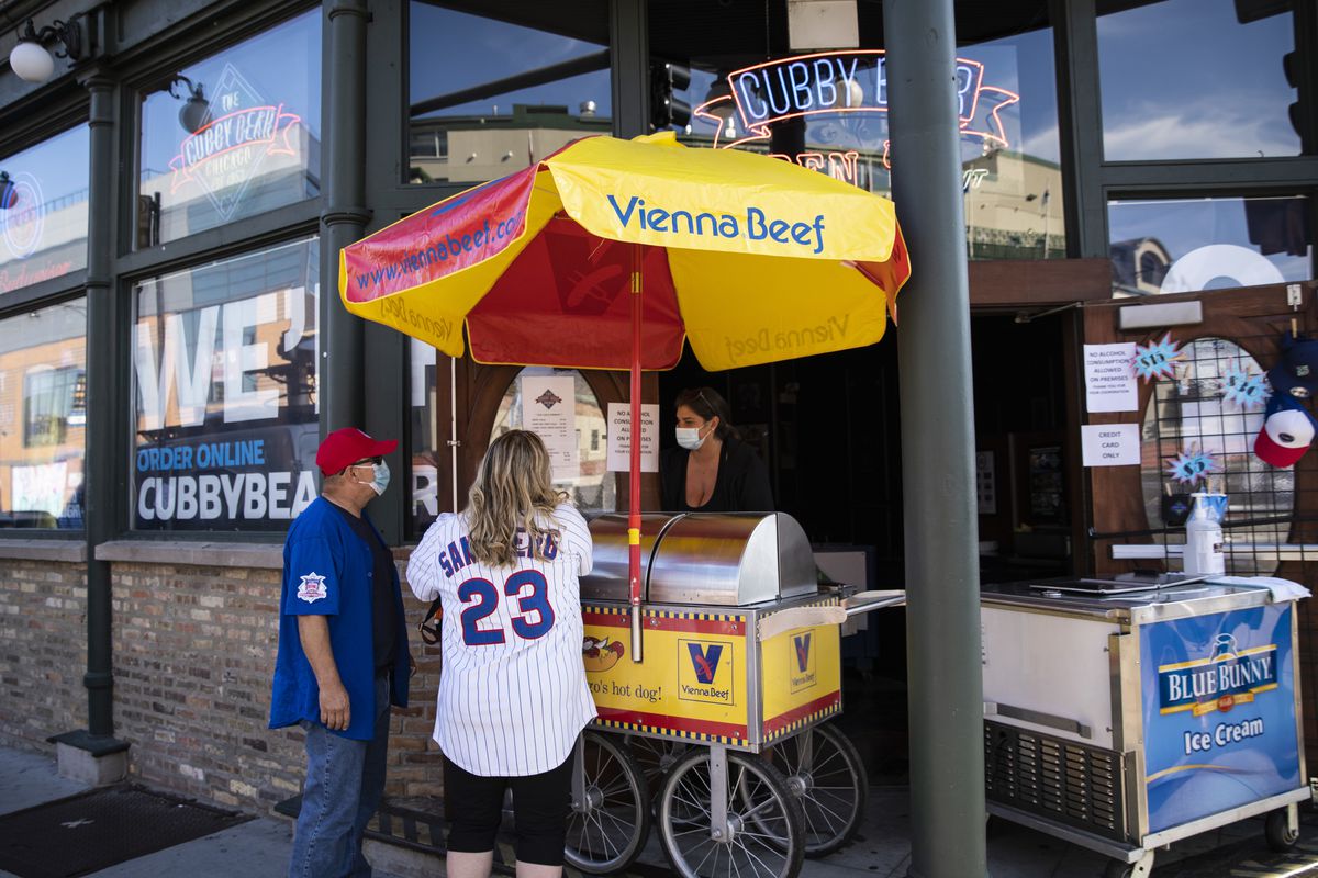The Cubby Bear serves people hot dogs and beer from the bar and restaurant’s doorway as guests aren’t allowed inside amid fears of the coronavirus pandemic as the Chicago Cubs take on the Milwaukee Brewers during the opening day game at Wrigley Field, Friday evening, July 24, 2020.