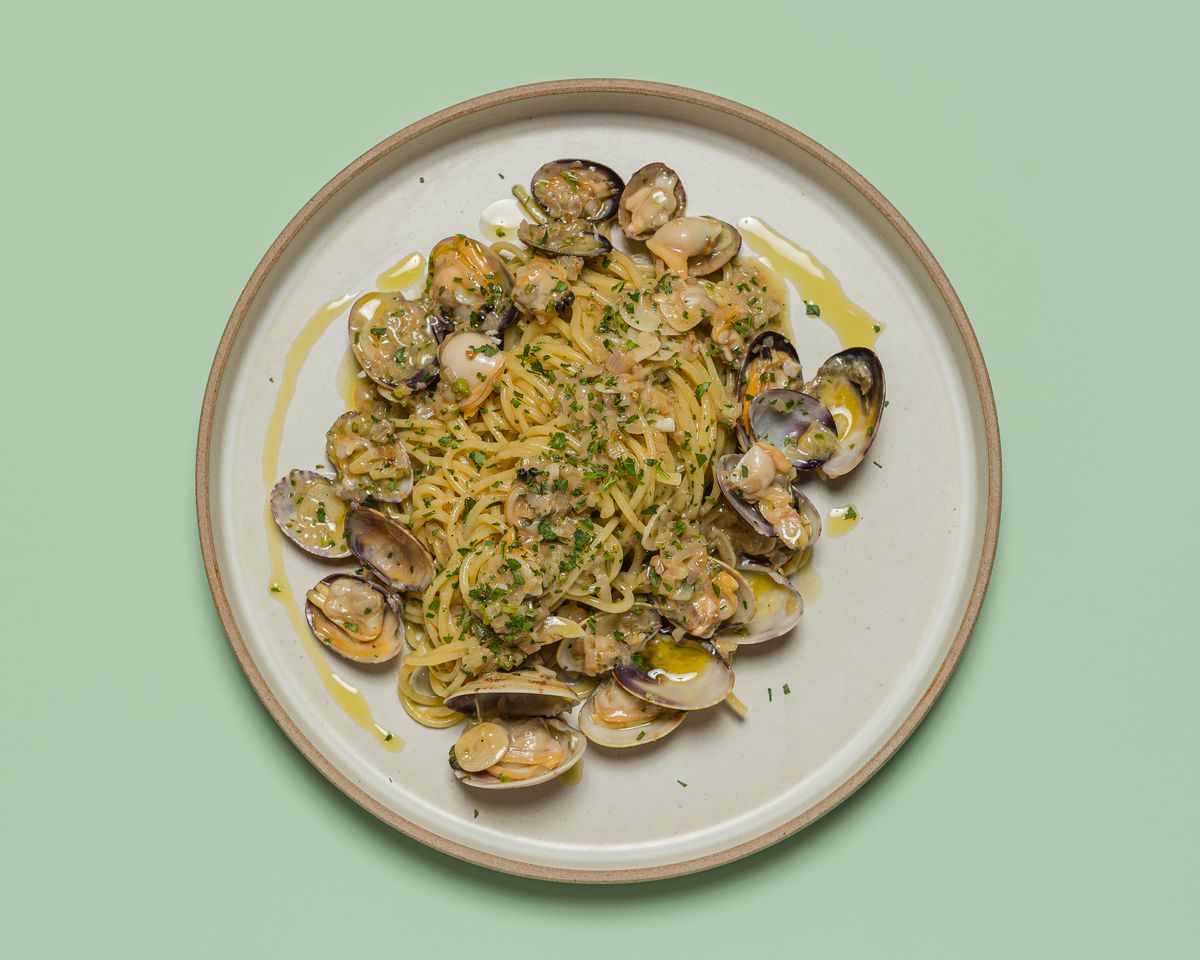Clams and pasta with lots of herbs shown from overhead against a green background at Mona Pasta Bar in Los Angeles.