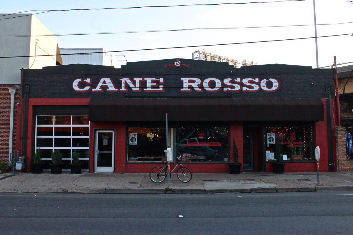 A red and black restaurant exterior with doors, windows, and an overhang that reads “Cane Rosso” in white letters.