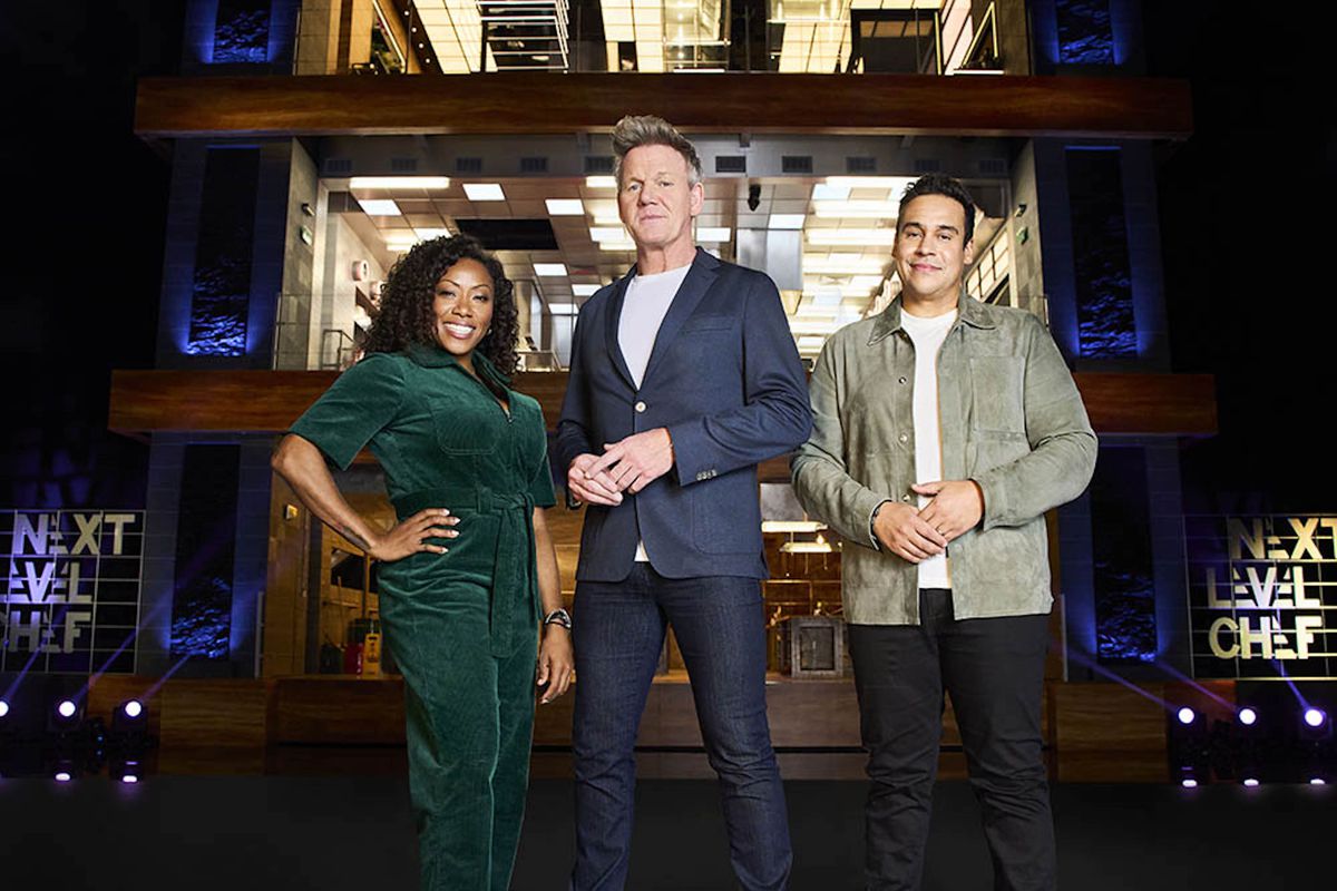 Next Level Chef judges Nyesha Arrington, Gordon Ramsay, and Paul Ainsworth stand in front of a three-level TV set, comprised of three different kitchens.