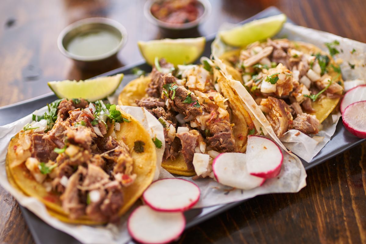Three tacos in yellow corn tortillas with meat and garnishes.
