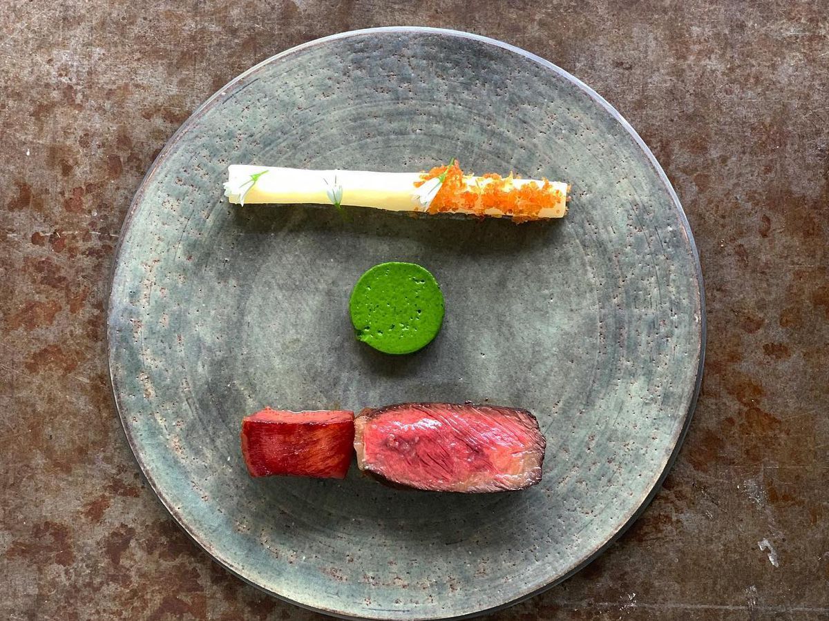 A grey ceramic plate, with a slice of rare beef, a green dollop, and a potato tube