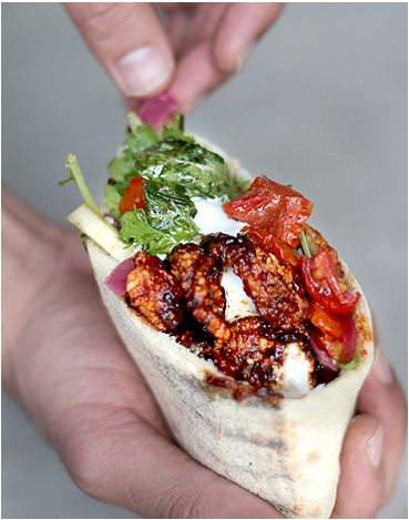 A hand holding a pita split and filled with meat, vegetables and sauces.