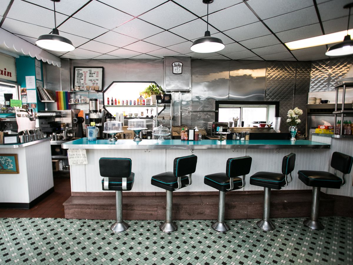 An empty counter with stools in a diner with retro decor including tiled floors and ceiling.