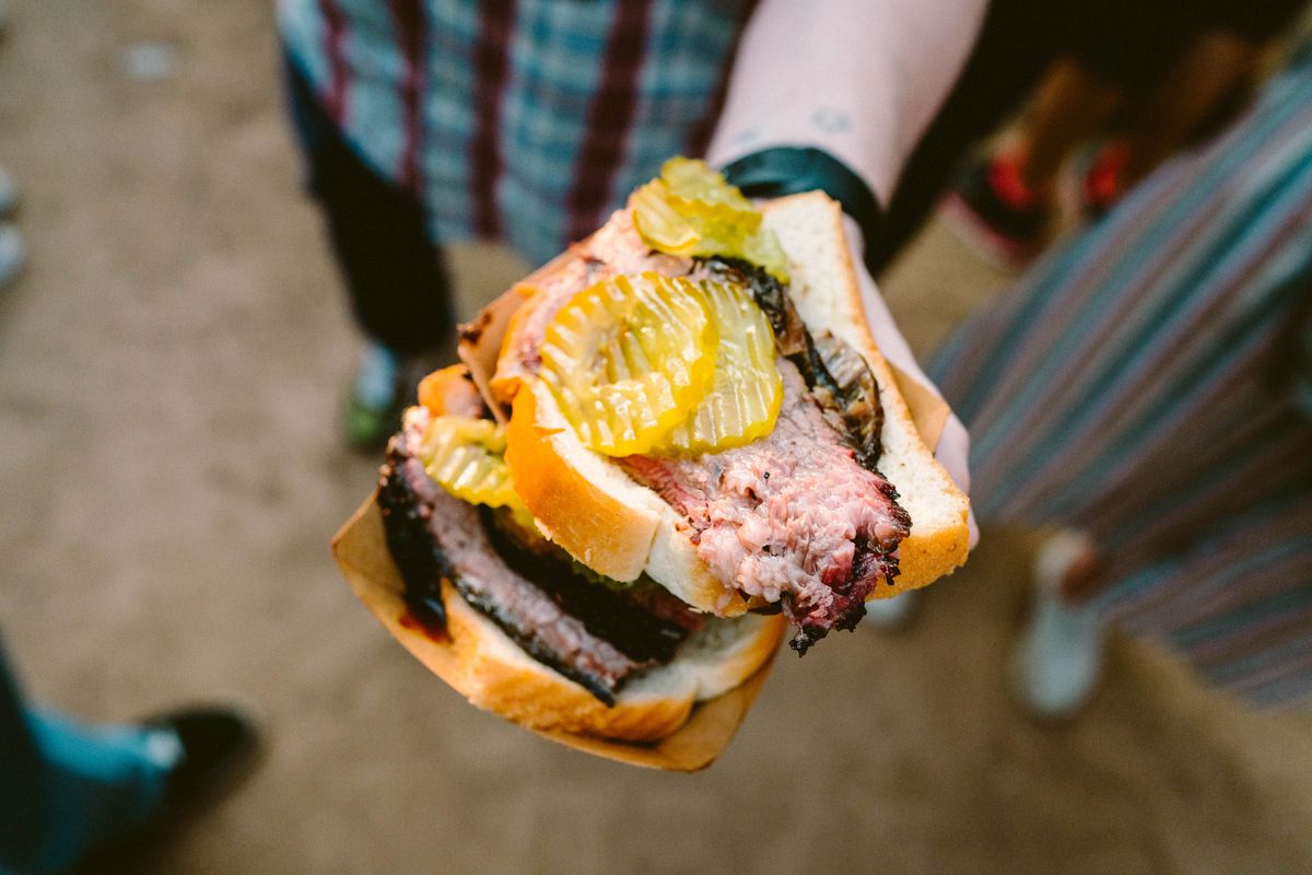 A person holding a brisket sandwich with sliced ​​pickles.