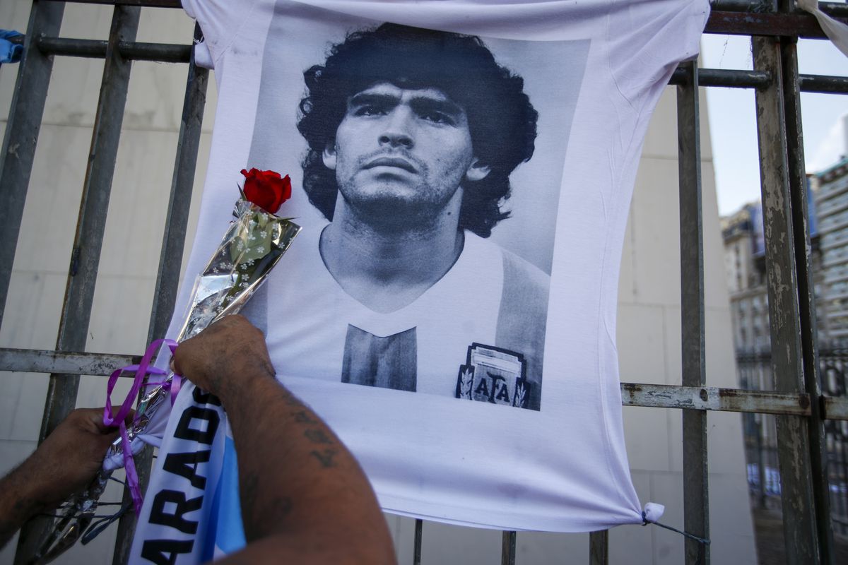 A man places a flower on a jersey with the face of late soccer star Diego Maradona in March. Seven health professionals who tended to Maradona in the days before his death have been charged with involuntary manslaughter.