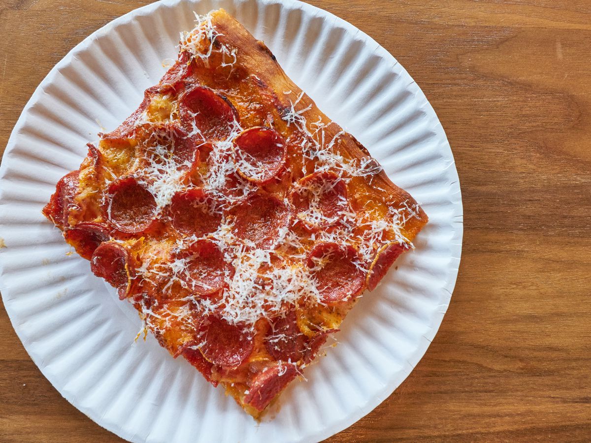A square cut of pepperoni pizza, sprinkled with grated parmesan, on a paper plate.