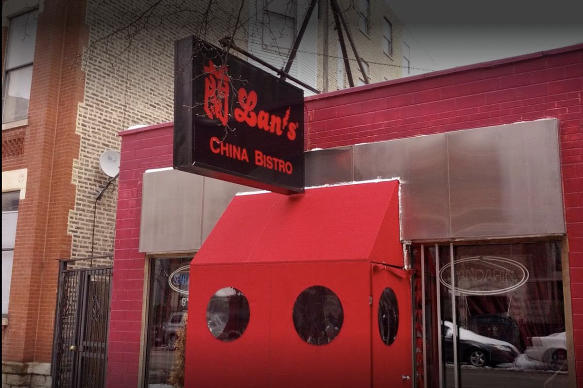 Snows on the ground outside a restaurant storefront with a sign and a red vestibule.