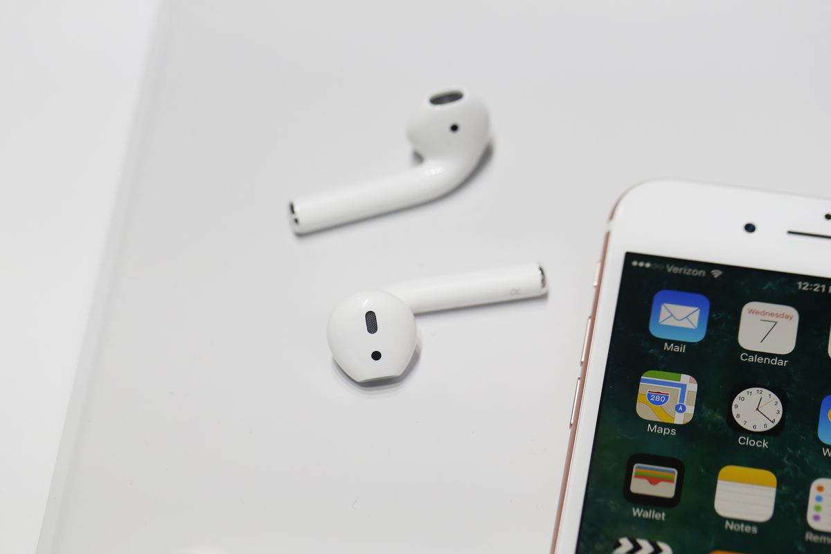 Two wireless AirPods — wireless earbuds — next to the iPhone 7 on a white background. They are white and shaped a bit like periscopes. The one on the bottom has some kind of design that looks like an exclamation point. 