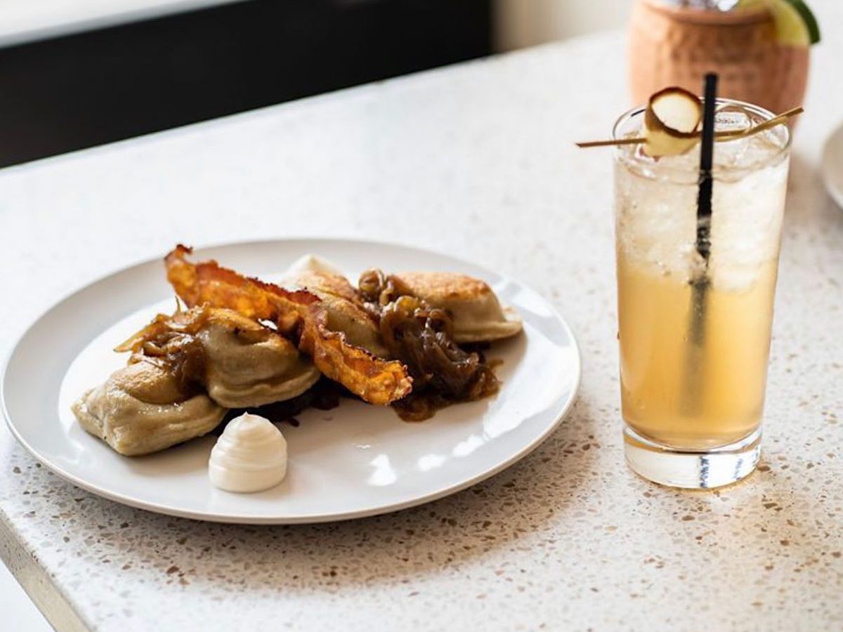 Plate of pierogi with bacon and onion alongside a cocktail