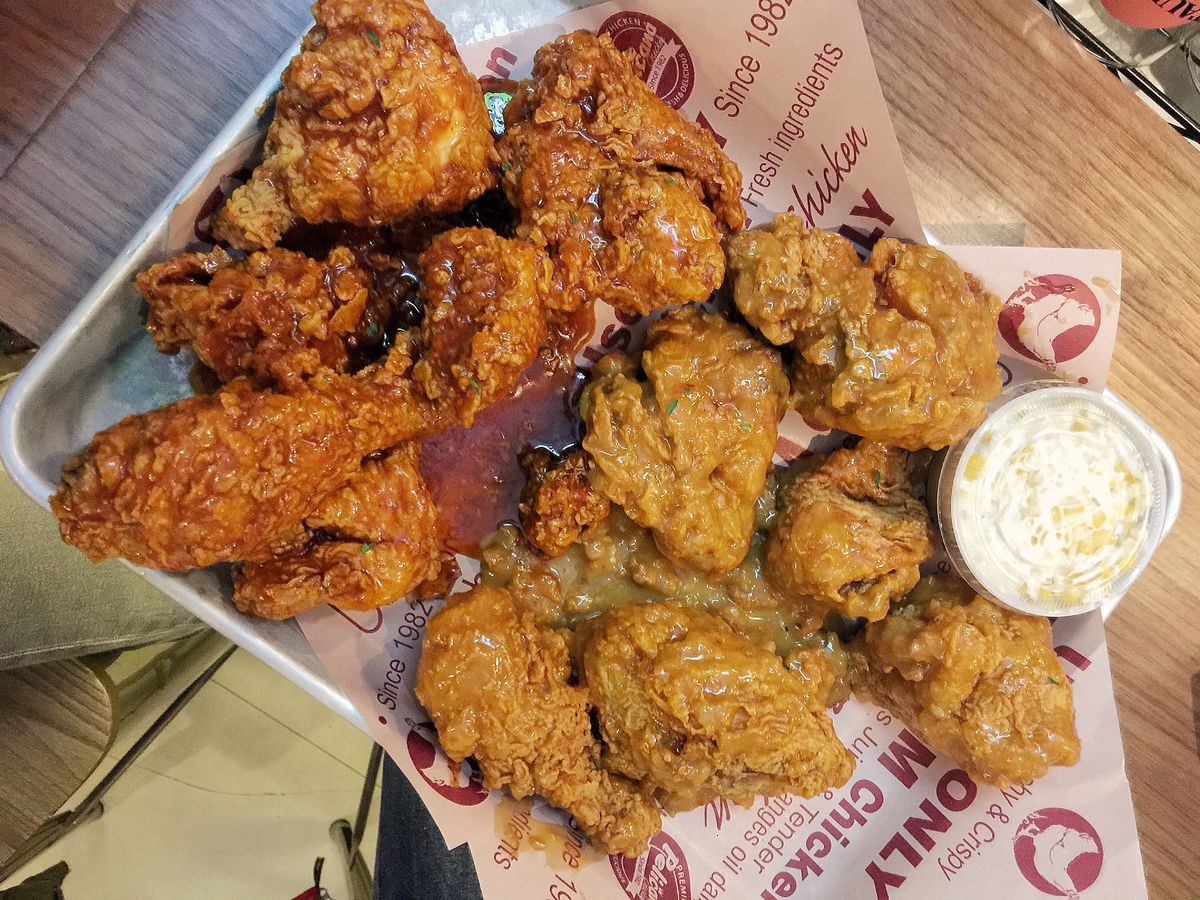 Assorted Pelicana fried chicken sits on a paper-lined metal tray