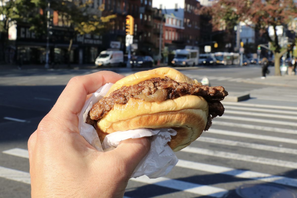 A hand holds a smash burger with American cheese and onions.