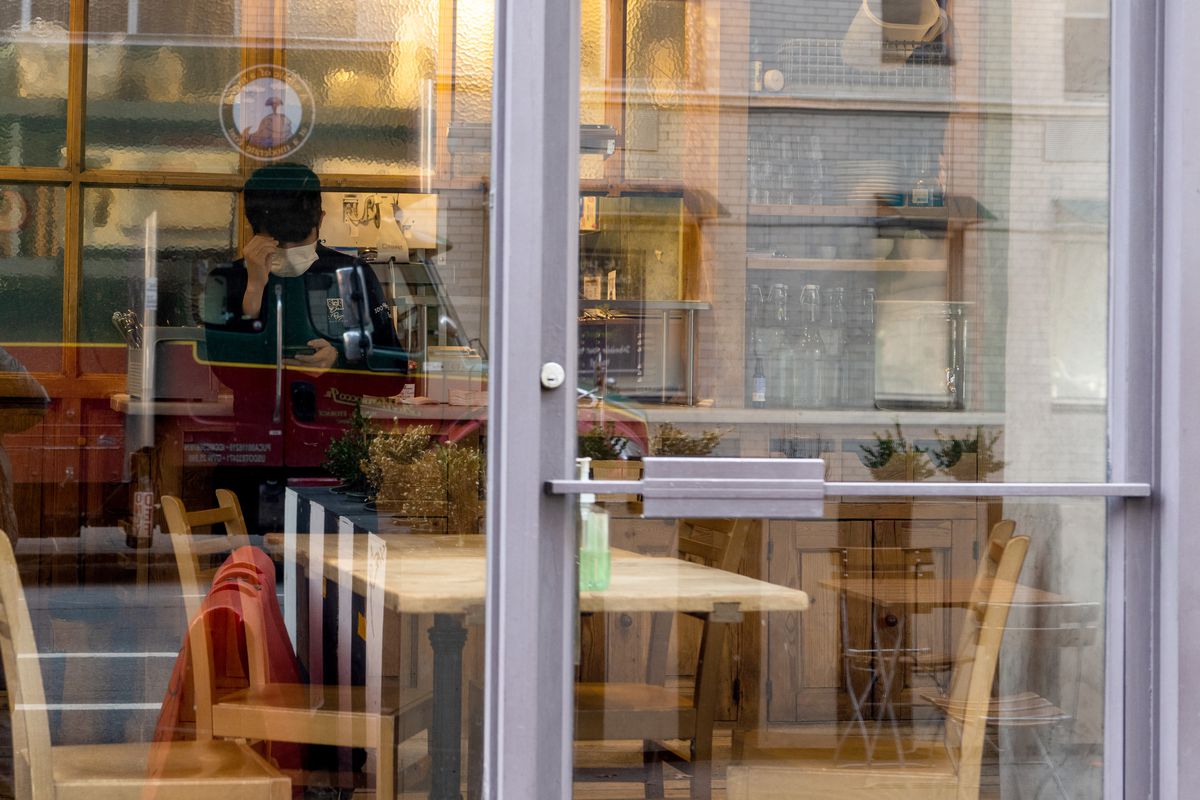 A waiter at Le Pain Quotiden wearing a mask looks at his phone near rows of empty tables during lunch hours.