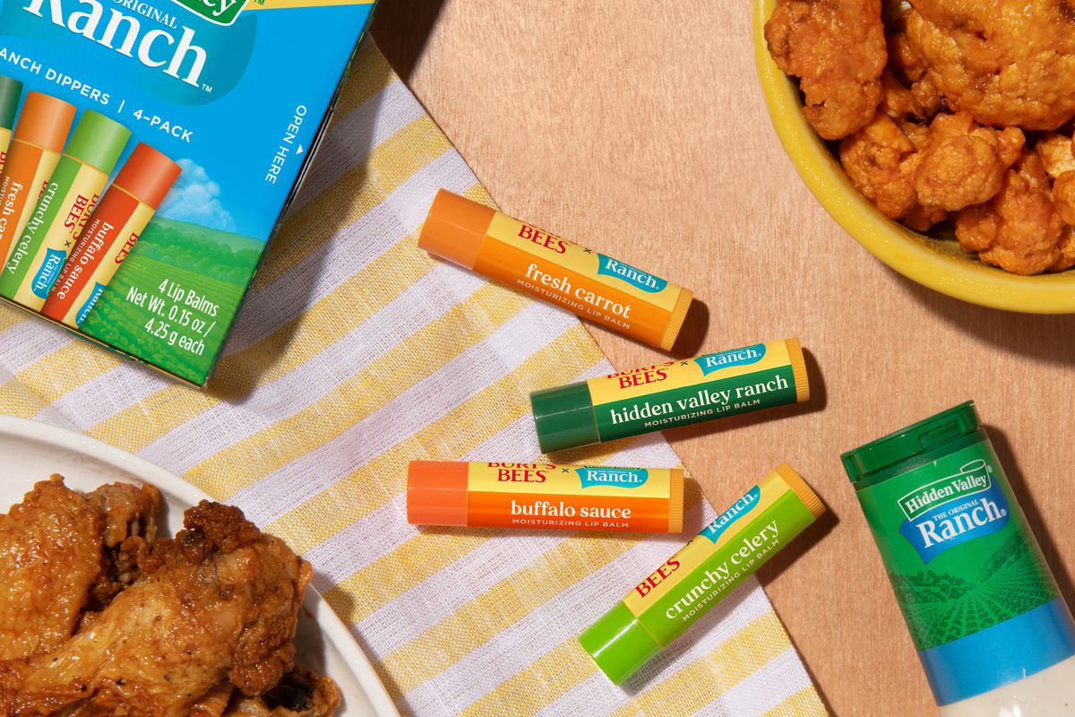 Four sticks of Hidden Valley x Burt’s Bees lip balm sit on a table with chicken wings.
