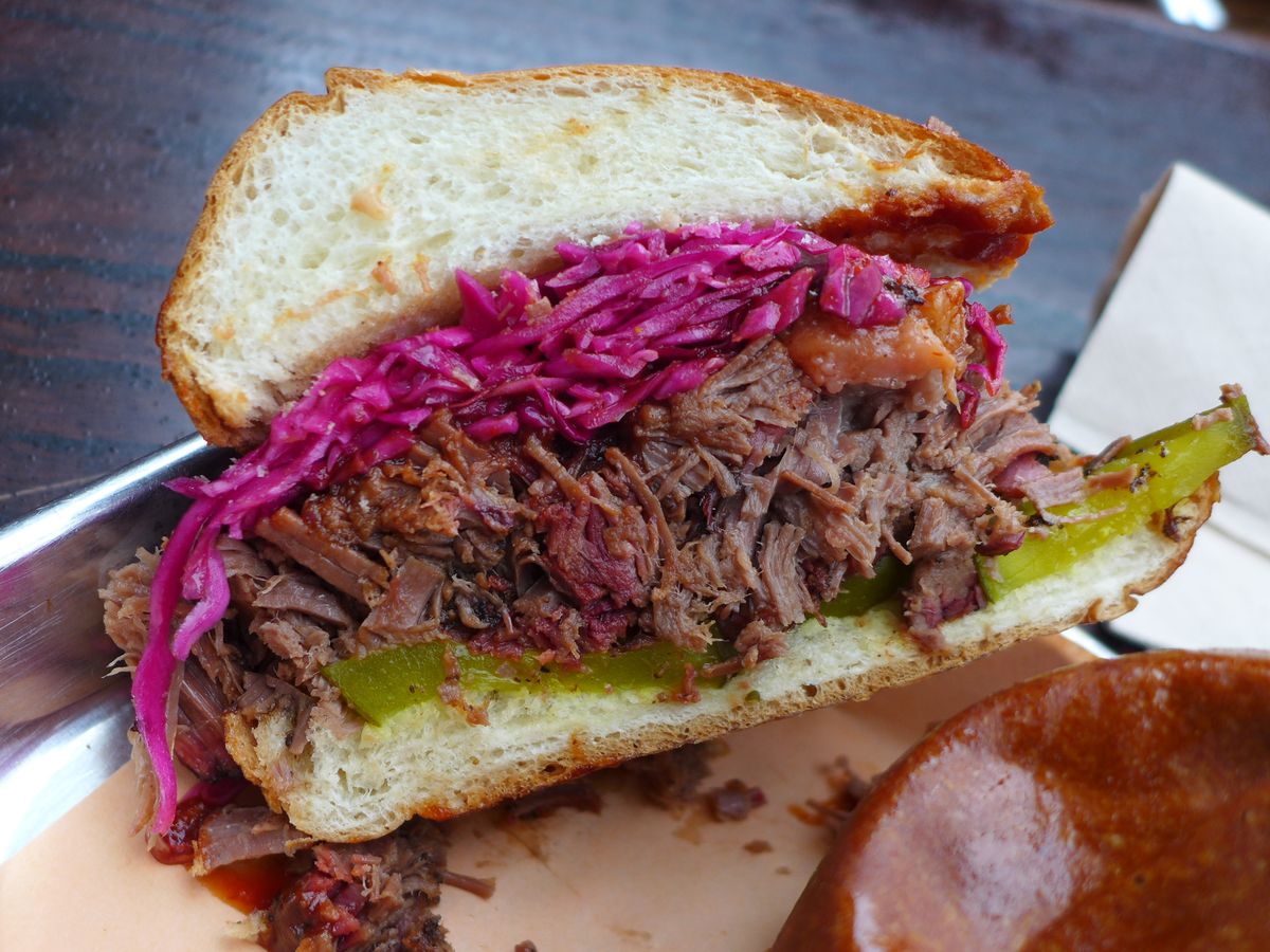 Brisket sandwich cut in half to show cross section, with purple cabbage slaw above the meat and a layer of pickled slices underneath.