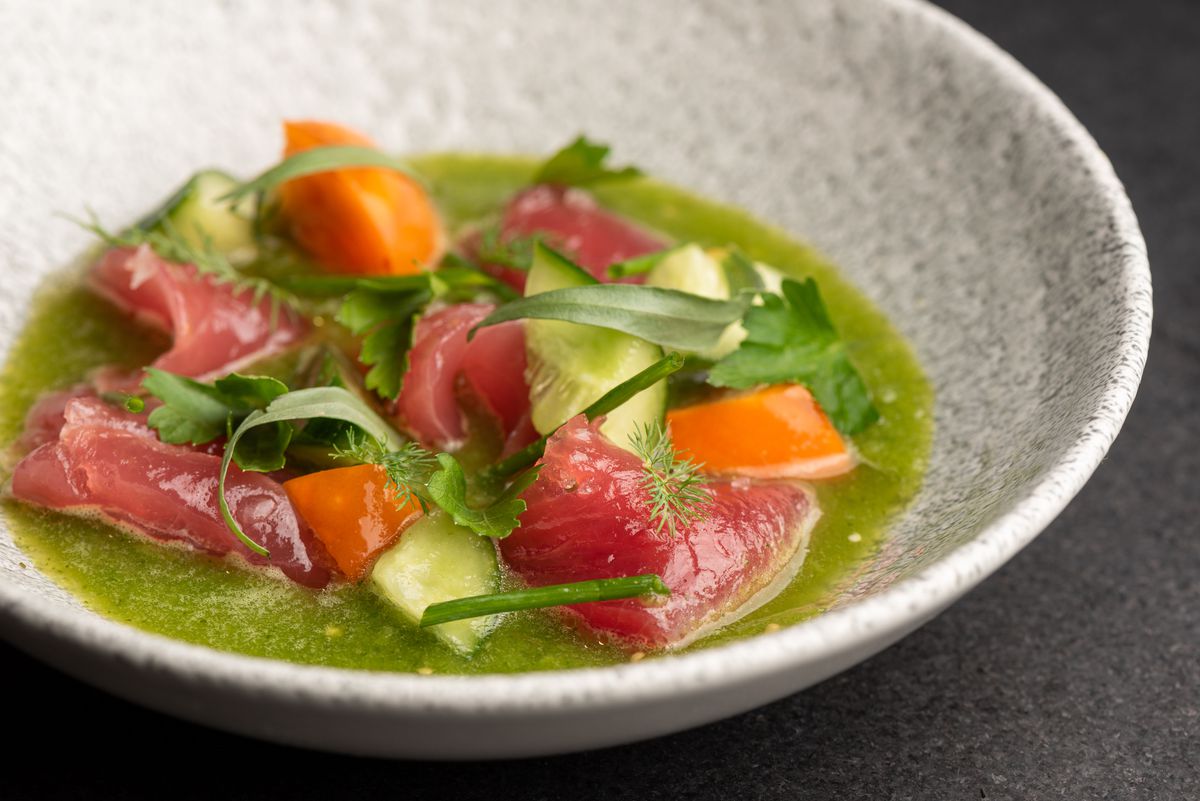 A close up photo of raw fish in green sauce in a bowl.