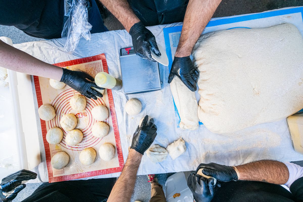 A bird’s eye view of hands from Z&amp;Z in black gloves cutting manoushe dough and forming it into balls