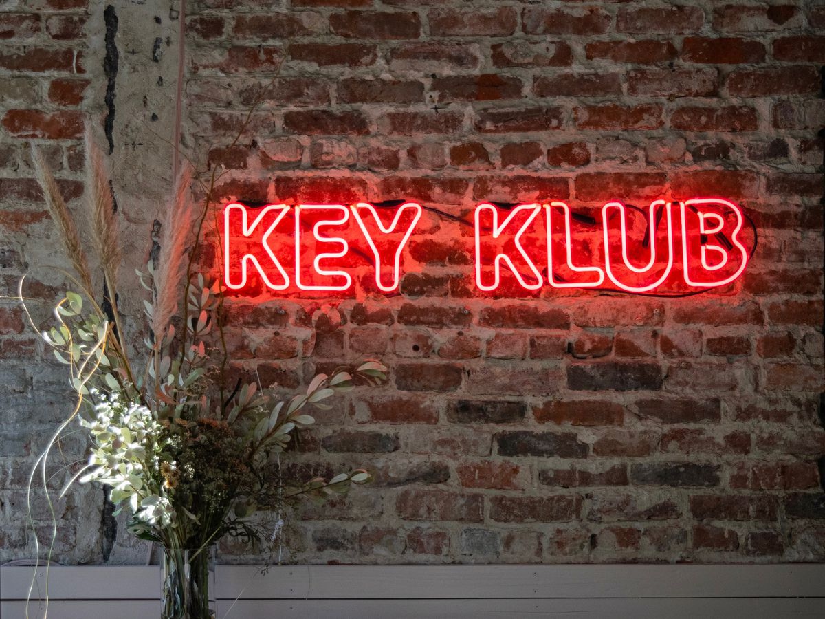 A red neon sign reading “Key Klub” on a brick wall.