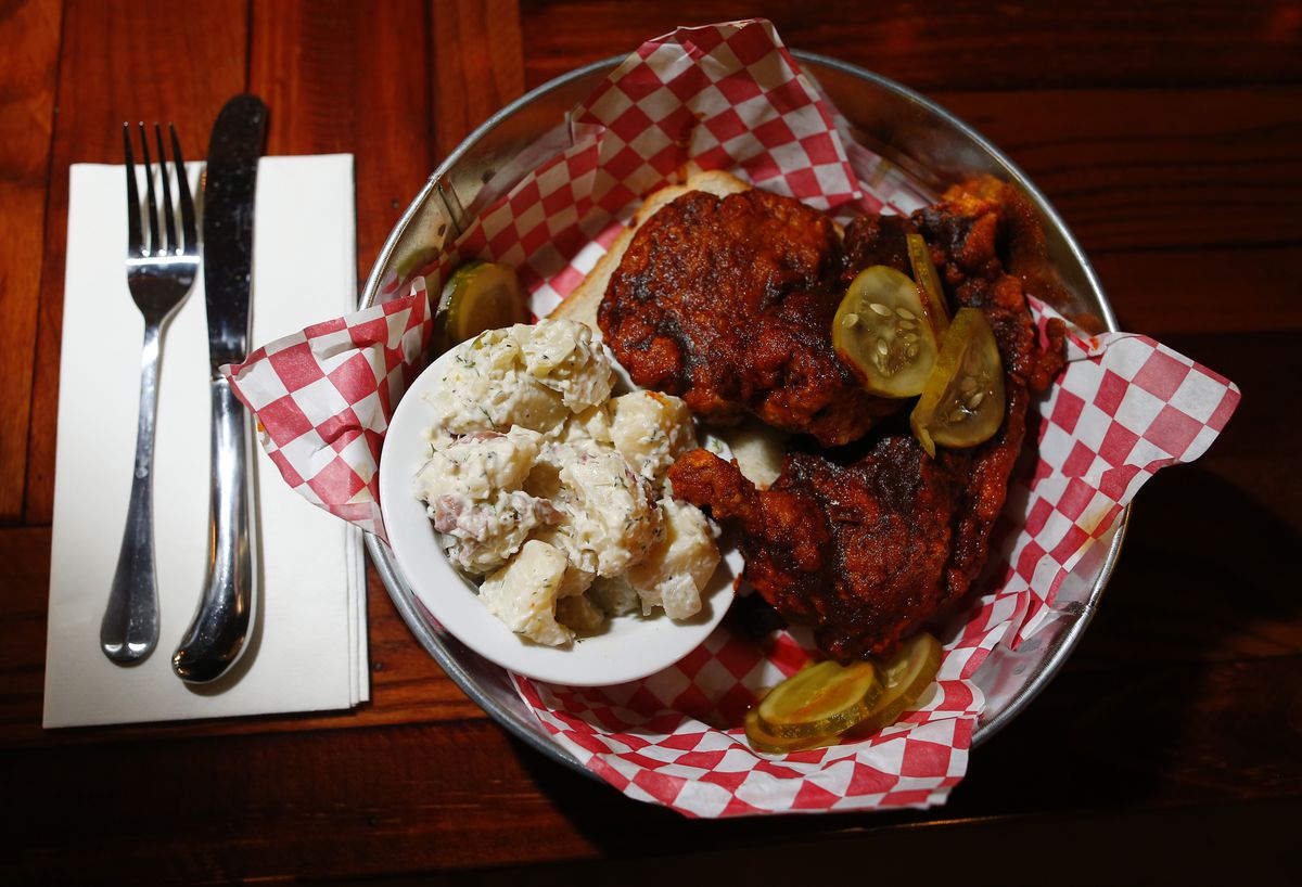 From above, a basket of fiery red hot chicken with potato salad and pickles. 