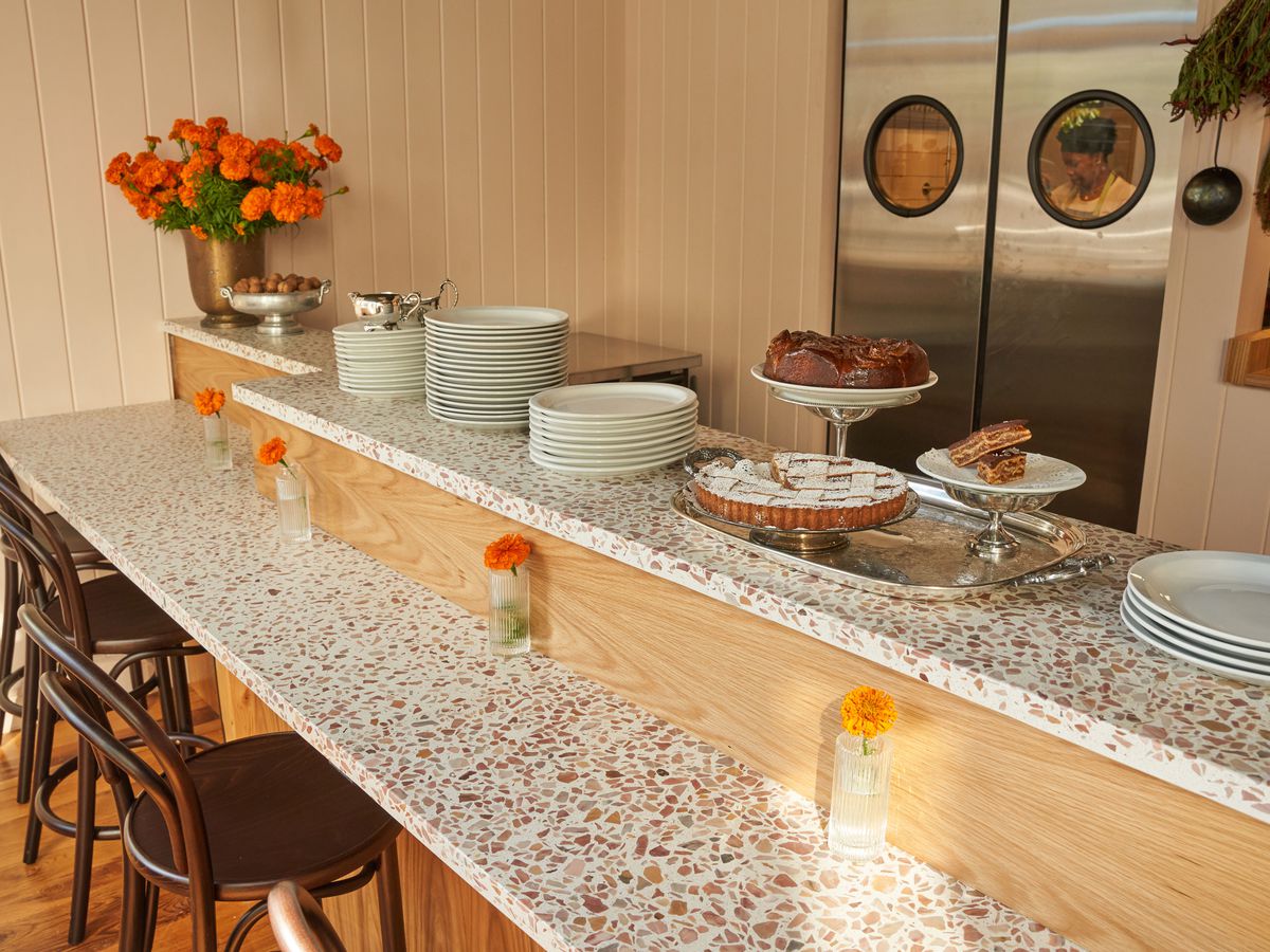 A bi-level terrazzo counter top has marigold flowers in vases and tiered plates featured pastries.