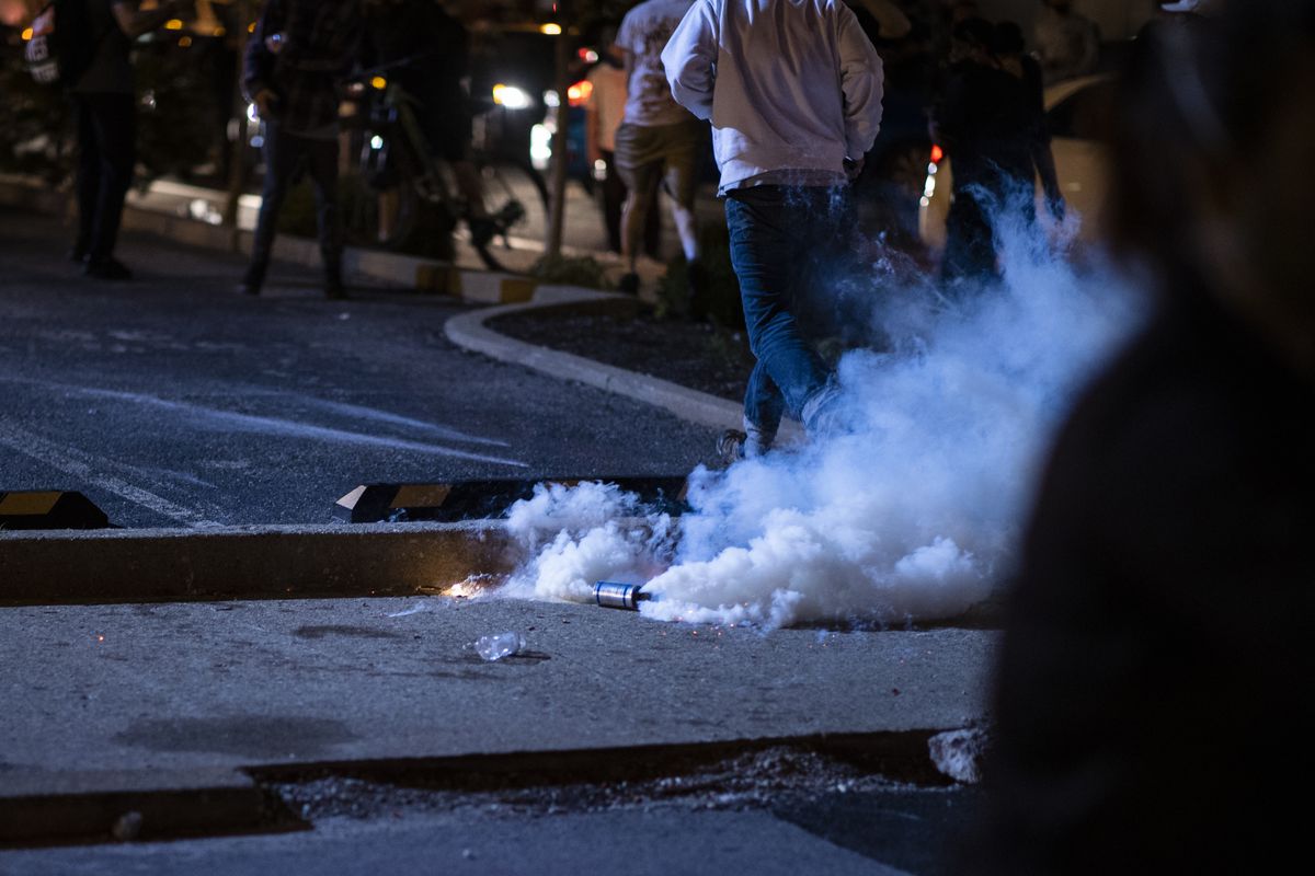 A man in a gray sweatshirt and blue jeans runs away from an active tear gas canister thrown by police on the street in Louisville.
