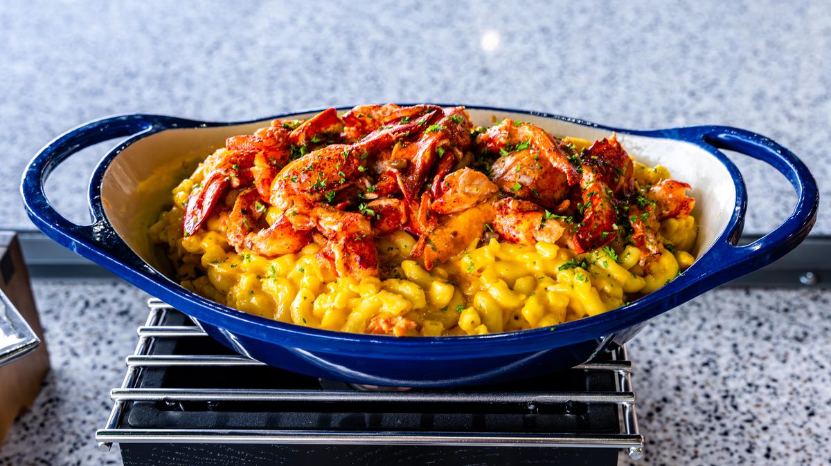 A blue bowl holds mac and cheese topped generously with lobster.