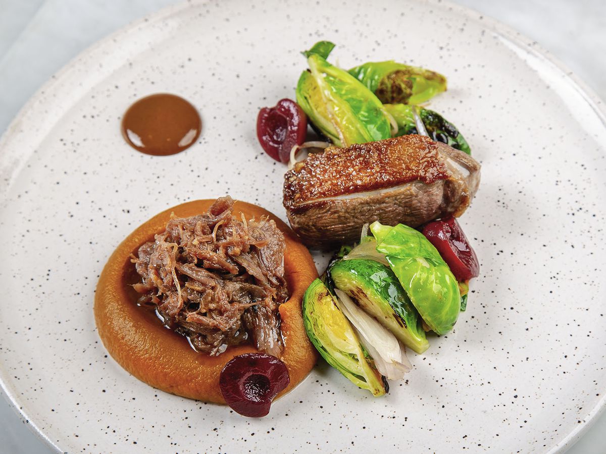 Goose served two ways, roasted and pulled in a pool of puree, with Brussels sprouts and dots of sauce on a speckled plate