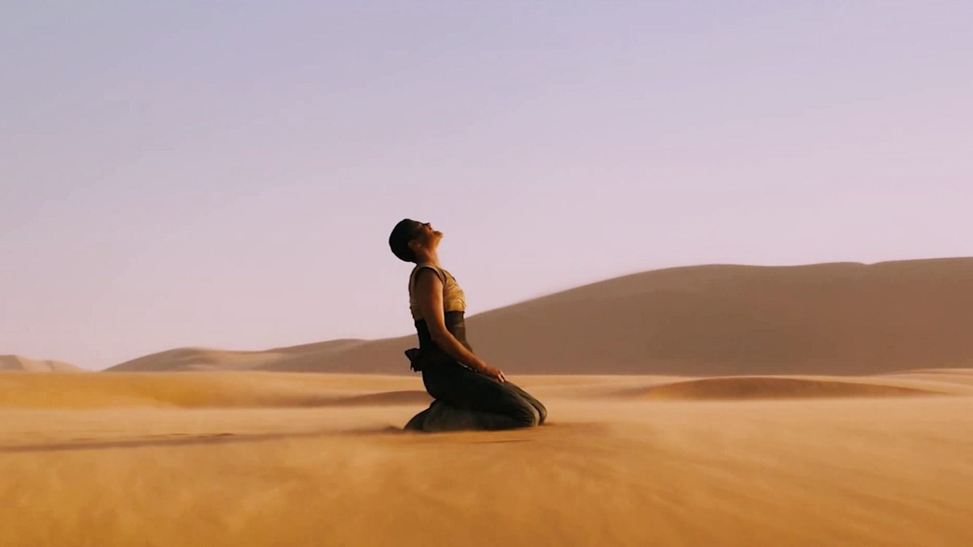 Imperator Furiosa (Charlize Theron) kneeling and looking up with pain in a desert in Mad Max: Fury Road