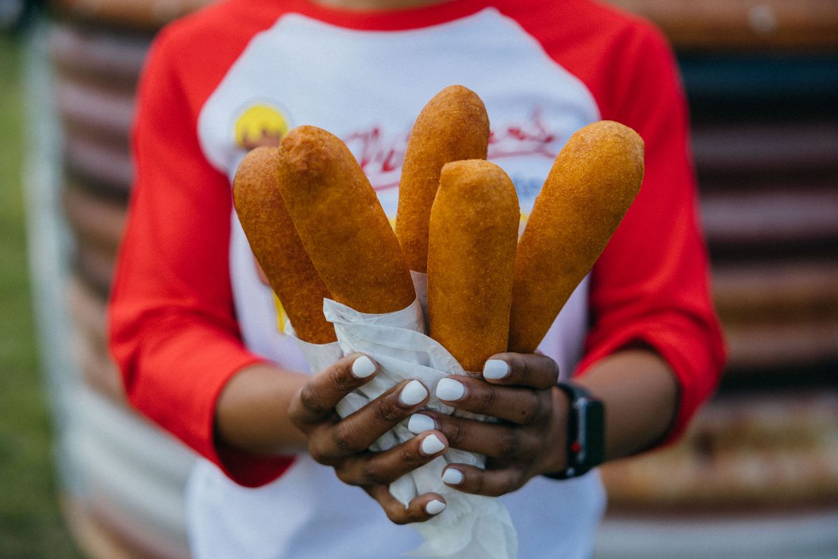 A person holds five corn dogs.