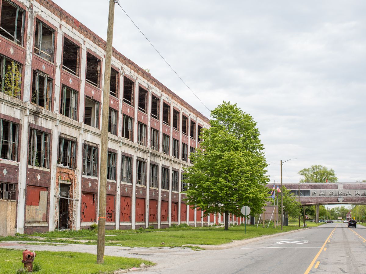 The exterior of an automotive plant in Detroit. The building has many windows and trees to the side of it.