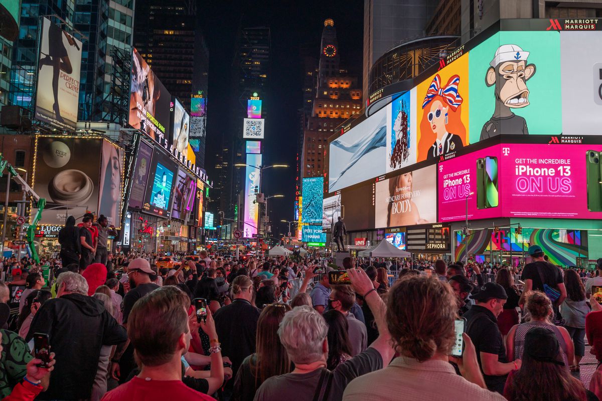 A crowd in Times Square with NFT images above them on billboards.
