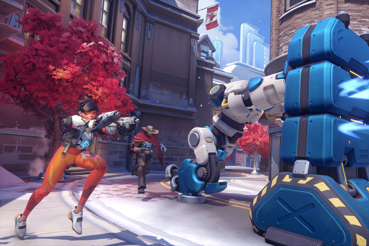 Tracer and Cassidy escort a robot pushing a large metal barrier in a screenshot from Overwatch 2’s Push mode, set on the Toronto map.