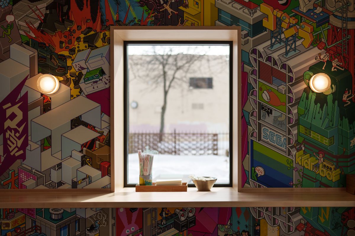A wall with a colorful motif wall paper and a window in the middle with a wooden counter attached.