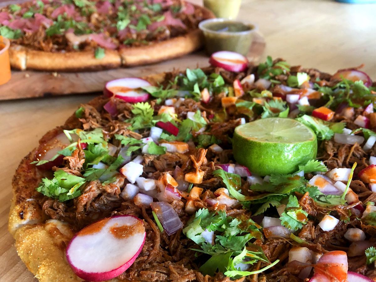 Two pizzas topped with birria.