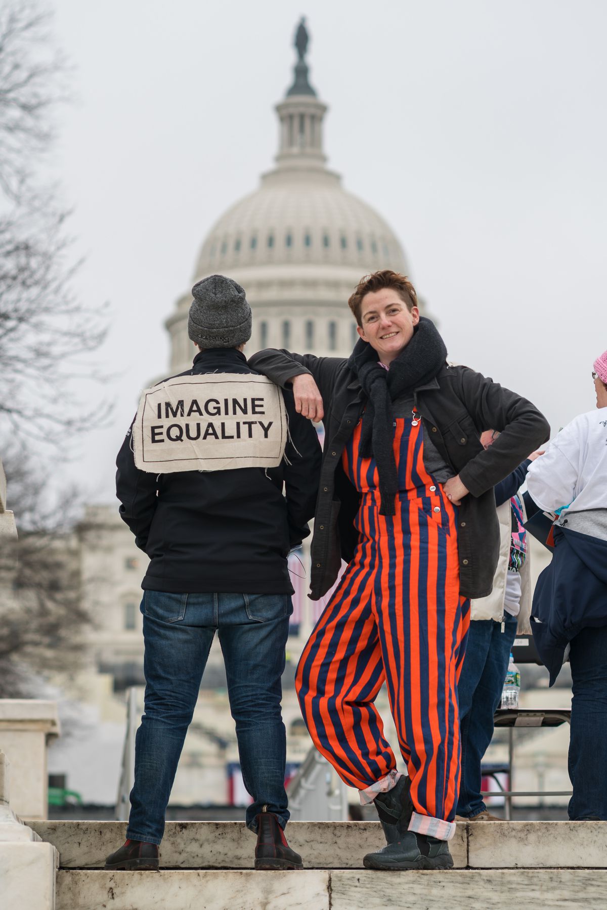A woman poses in orange and navy striped overalls in front of the Capitol building.