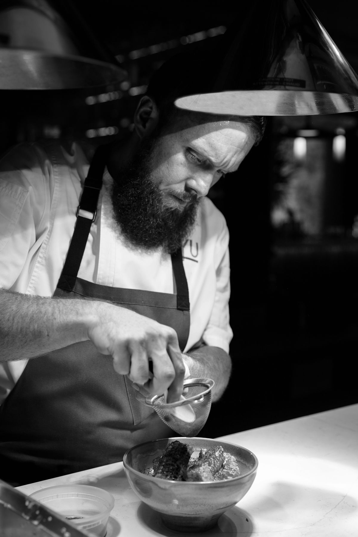 A black and white photo of a chef adding a garnish to a dish.