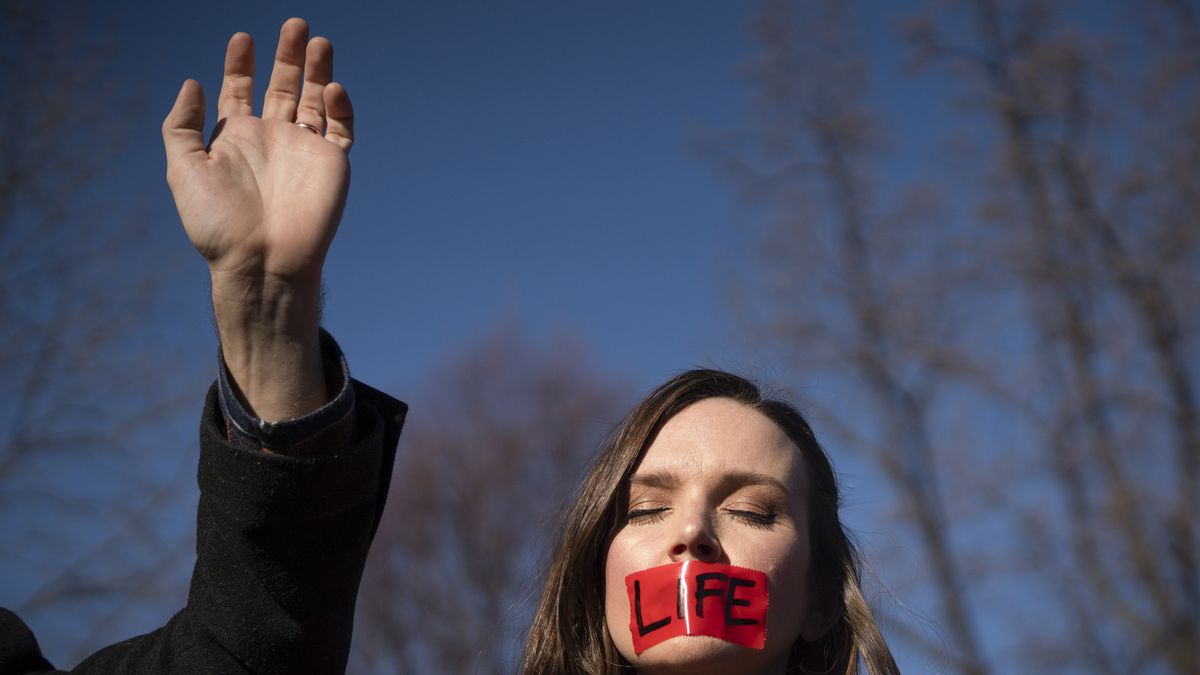 An anti-abortion protester with red tape over her mouth reading “Life.”