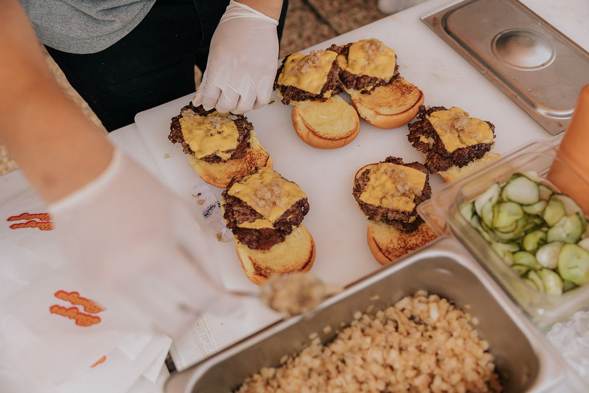 A person at Burger Bodega decorates cheeseburger patties with toppings at Have a Nice Day Market.