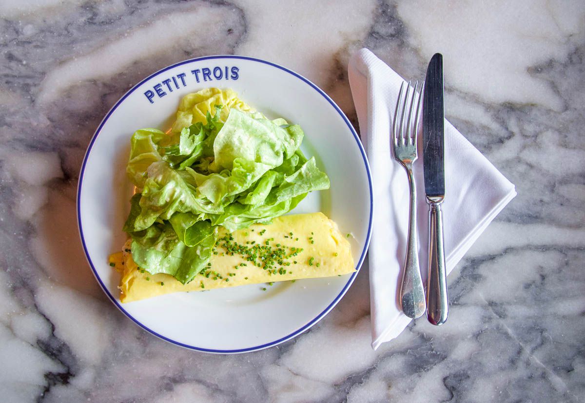 An omelet served with lettuce on top with a place setting, at a tabletop at Petit Trois in Los Angeles. 