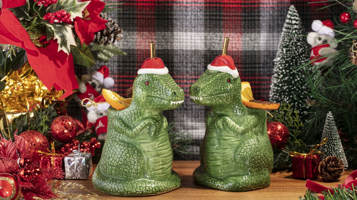 Two dinosaur with santa hat shaped cups. With ornaments in the background.