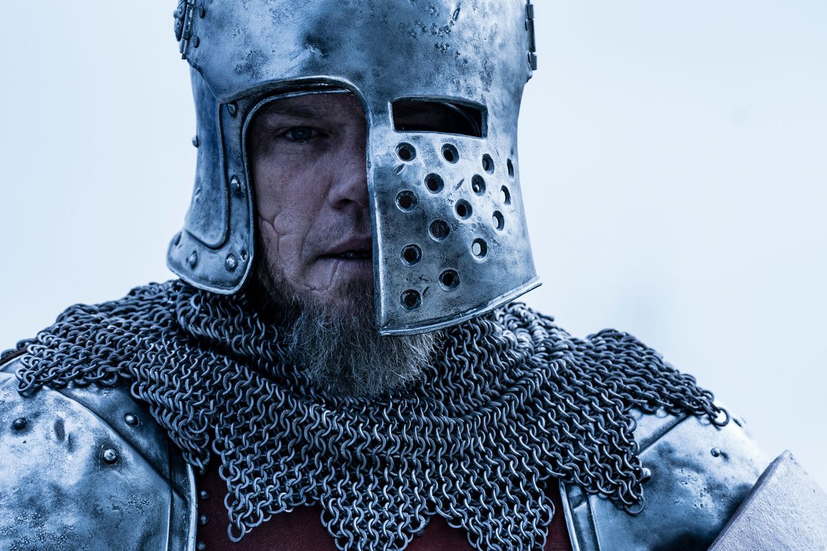 Matt Damon with a scarred face and a battered helmet covering half his head in The Last Duel