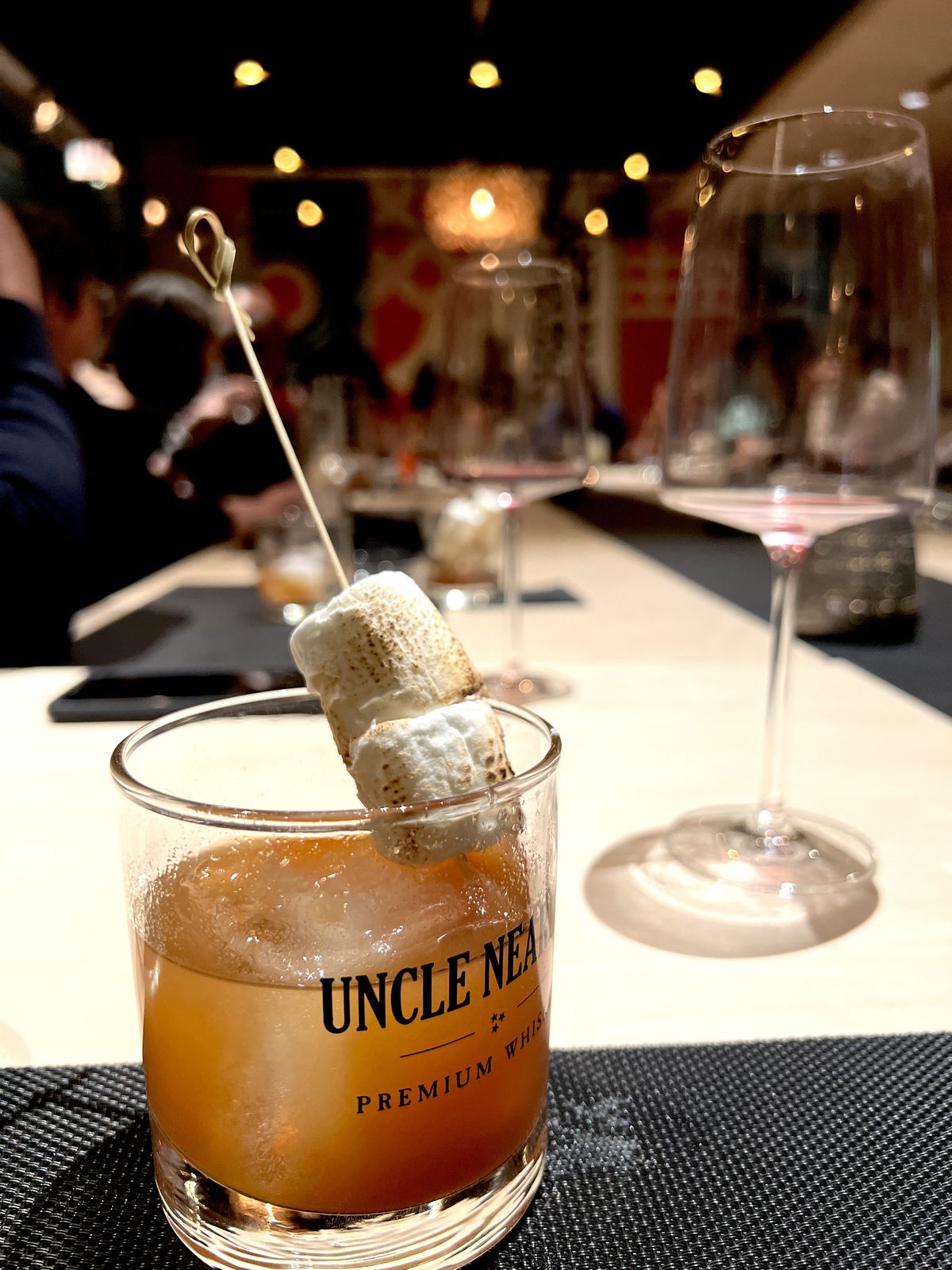 A glass with brown liquor and a garnish of marshmallow.