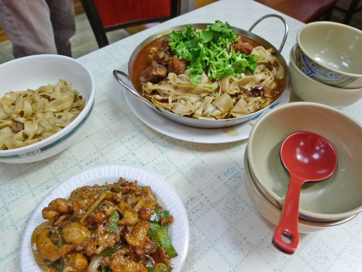 A variety of dishes including a wok with hot red oil and chicken, a bowl of noodles, and an inscrutable other dish.