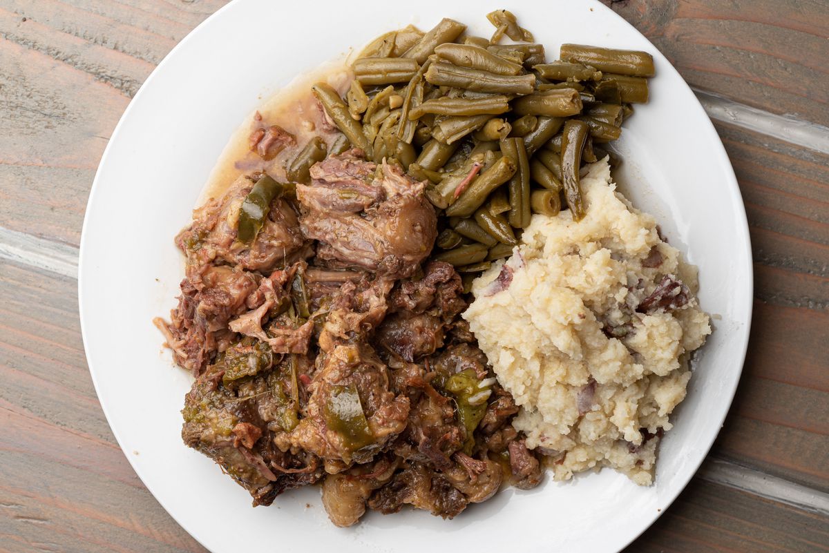 A plate of stewed oxtails with mashed potatoes and green beans.