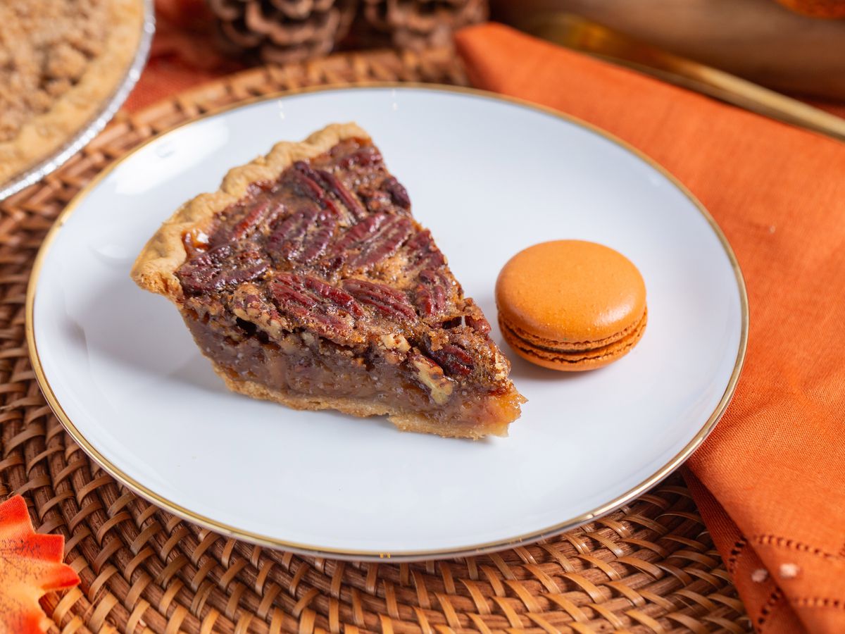 A slice of pecan pie sits on a plate with a pumpkin-flavored macaroon.