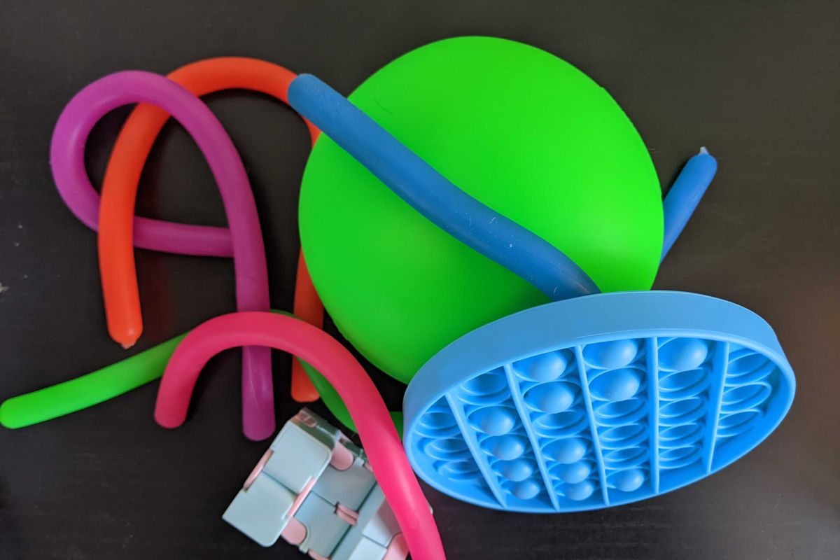 A pile of bright, neon colored fidget toys. Some are long rubber noodles, there’s a giant neon green stress ball, a push pop bubble, and an infinity cube. 