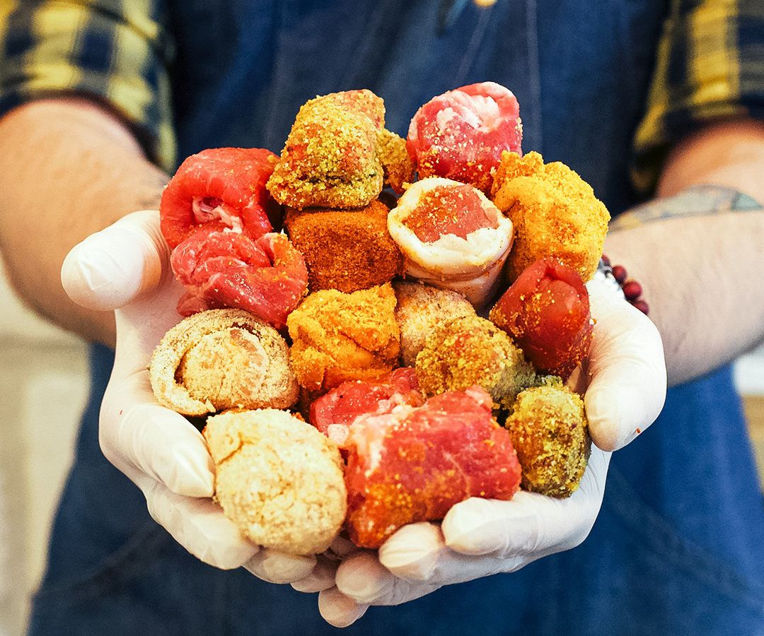 A chef holds out a pile of colorful bombette in gloved hands