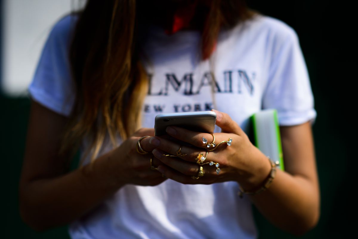 Girl in Balmain T-shirt reading on her phone
