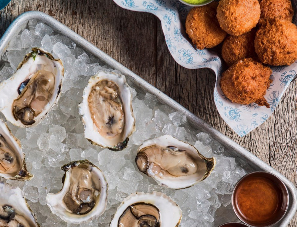 From above, oysters on a bed of ice with sauces, beside a basket of hush puppies.